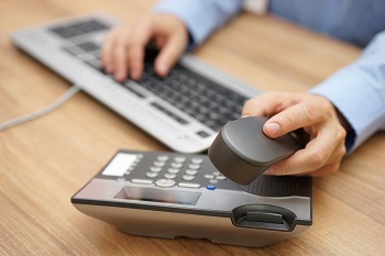 man with hand on keyboard and the other picking up a desk phone